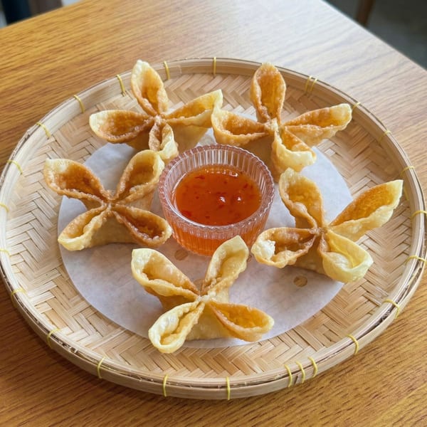 Six golden-fried crab rangoons arranged around a small bowl of sweet chili sauce on a bamboo tray.