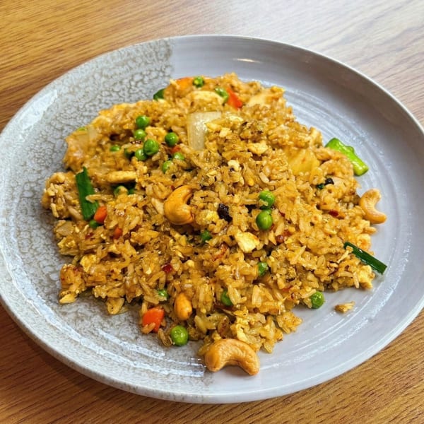 Golden fried rice with peas, cashews, and chicken on a grey plate.