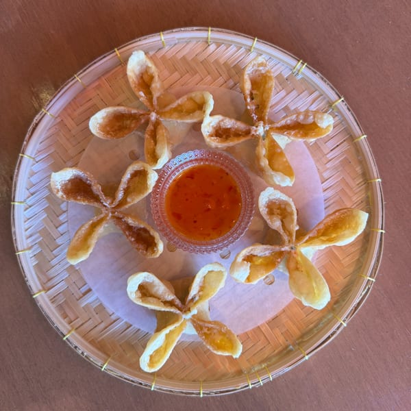 Flower-shaped fried wontons with a small bowl of chili dipping sauce on a woven tray.