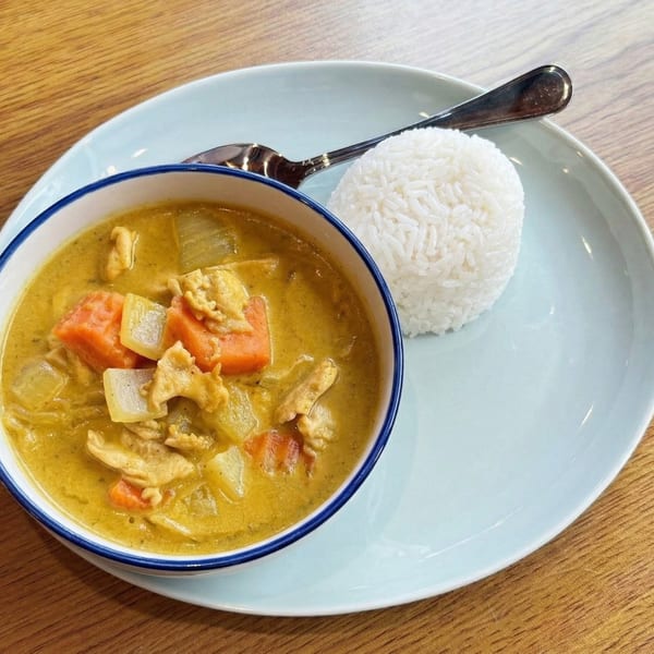 Yellow curry with chicken, carrots, and onions in a bowl, served with white rice and a spoon.