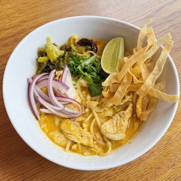 Close-up of a bowl of Khao Soi with chicken, noodles, red onion, lime, and crispy wontons.