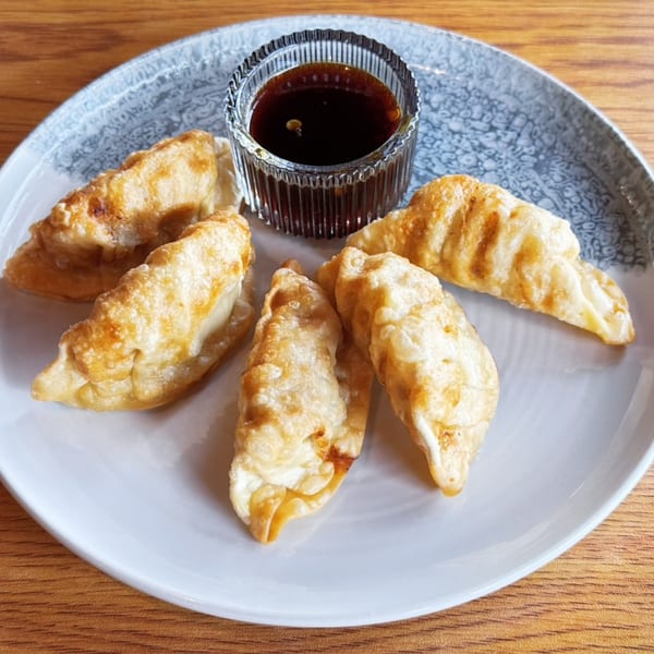 Five golden-fried dumplings arranged around a small glass bowl of dark dipping sauce on a plate.