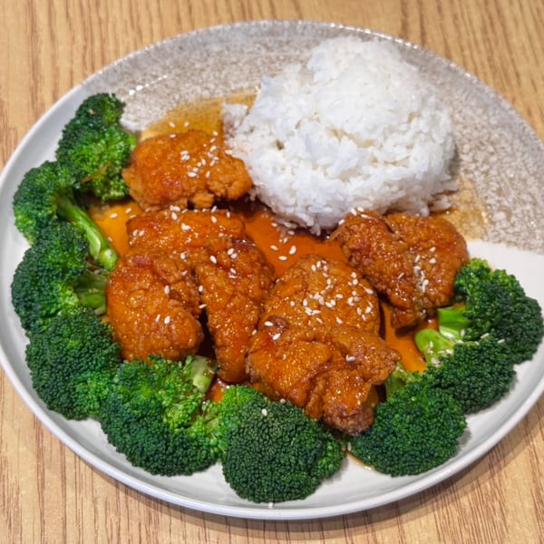 Orange chicken with sesame seeds, white rice, and broccoli florets on a white plate.