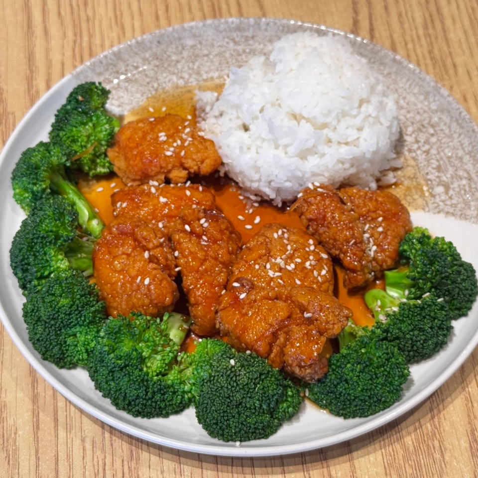 Orange chicken with sesame seeds, white rice, and broccoli florets on a white plate.